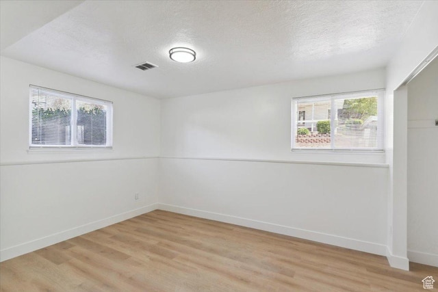 spare room with light wood-style floors, a healthy amount of sunlight, visible vents, and a textured ceiling