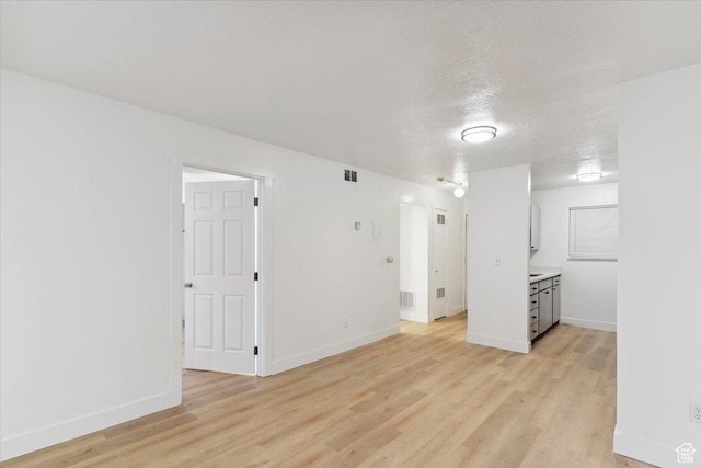 interior space featuring baseboards, light wood-style flooring, visible vents, and a textured ceiling