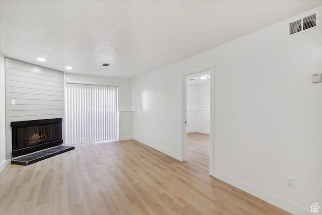 unfurnished living room with light wood finished floors, a large fireplace, visible vents, and baseboards