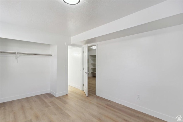 unfurnished bedroom featuring a closet, light wood-style floors, baseboards, and a textured ceiling