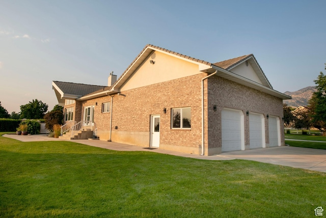 105 S 400 E, Hyde Park, UT 84318 - property exterior at dusk featuring an attached garage, brick siding, concrete driveway, a chimney, and a lawn