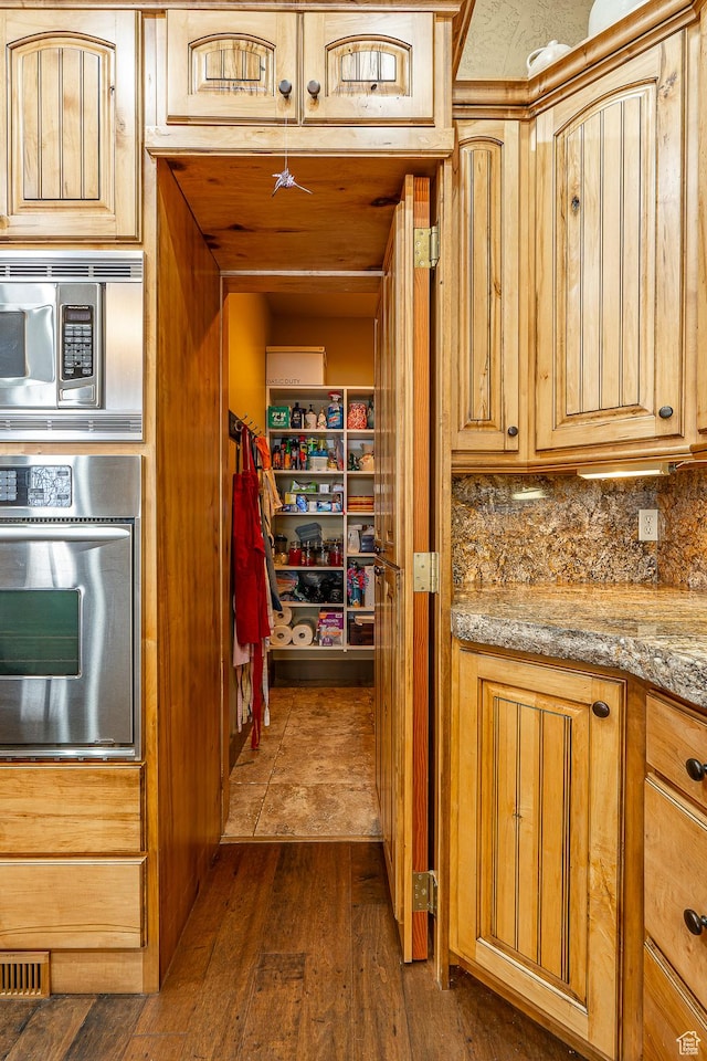 kitchen featuring light brown cabinets, light stone countertops, dark wood-style flooring, tasteful backsplash, and appliances with stainless steel finishes