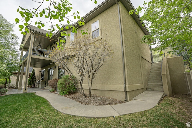 back of property with stairs, a balcony, stucco siding, ceiling fan, and a lawn