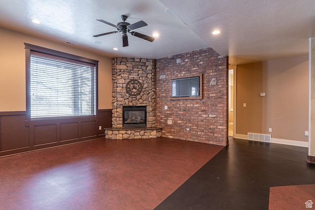 unfurnished living room featuring a stone fireplace, visible vents, wainscoting, and ceiling fan