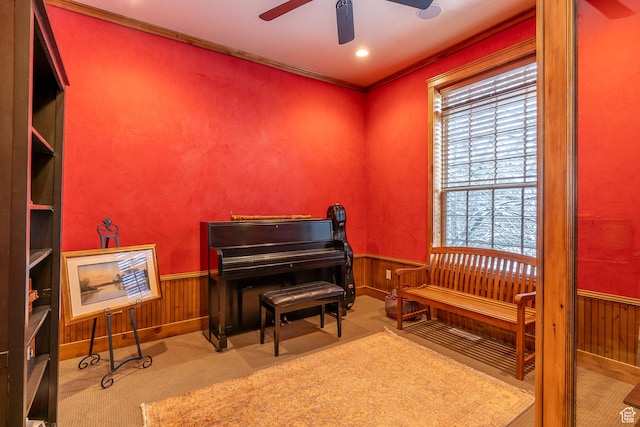 sitting room featuring carpet, ceiling fan, wood walls, crown molding, and a wainscoted wall