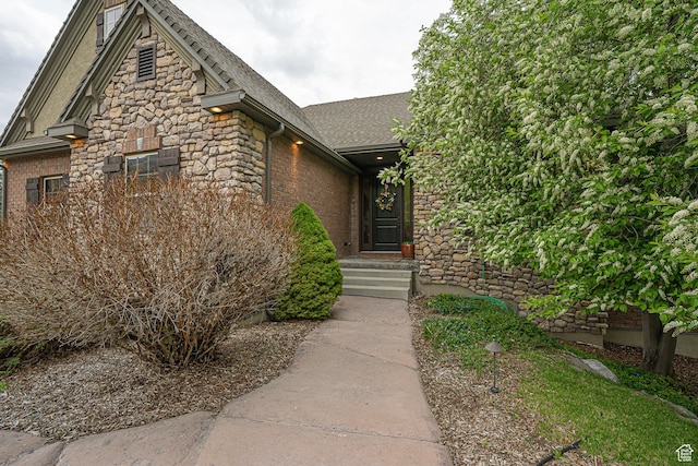 entrance to property featuring a shingled roof and stone siding
