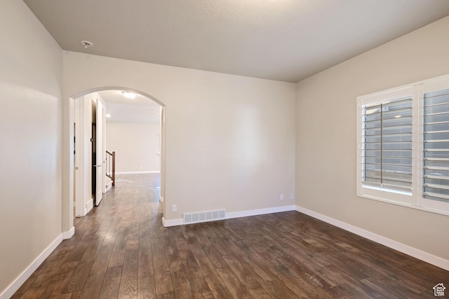 spare room featuring visible vents, baseboards, arched walkways, and dark wood-style floors