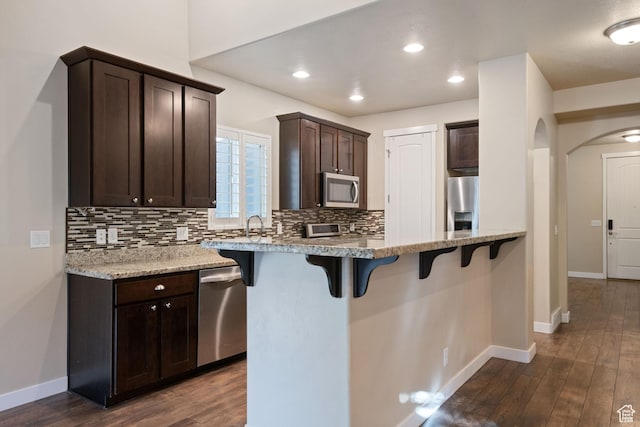 kitchen with a breakfast bar area, backsplash, dark brown cabinets, and appliances with stainless steel finishes