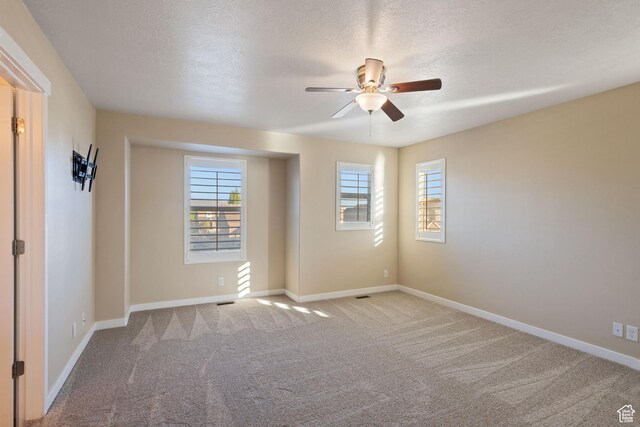 carpeted empty room with a textured ceiling, baseboards, and a ceiling fan
