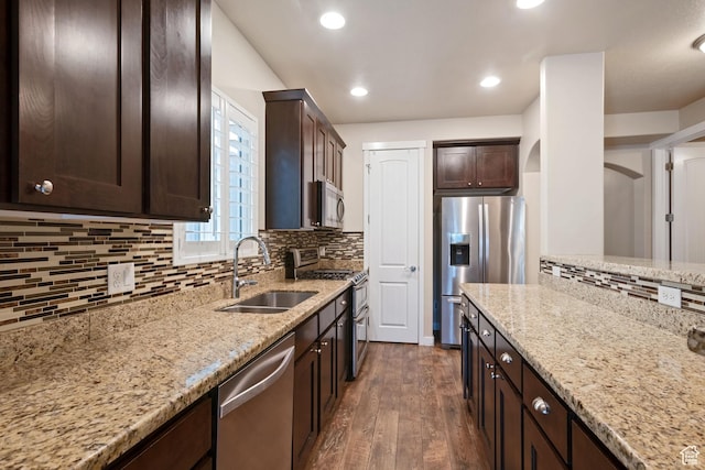 kitchen with light stone counters, a sink, dark brown cabinetry, stainless steel appliances, and dark wood-style floors