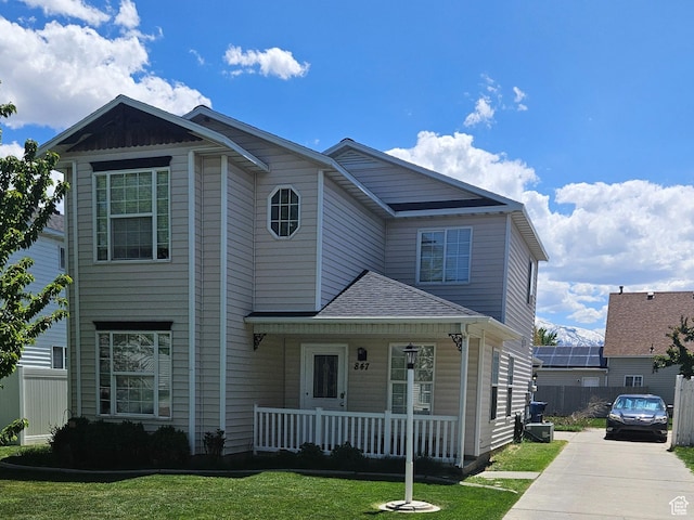 view of front of home with covered porch, fence, concrete driveway, a shingled roof, and a front yard