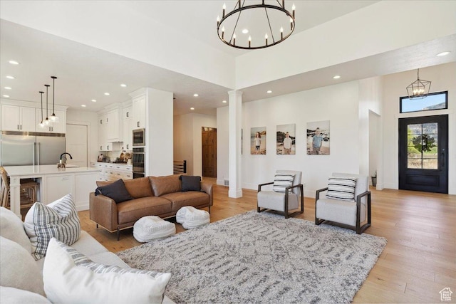 living room with an inviting chandelier, light wood-type flooring, ornate columns, and recessed lighting