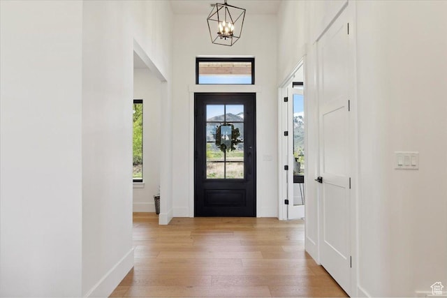 entryway featuring a chandelier, a high ceiling, baseboards, and light wood-type flooring
