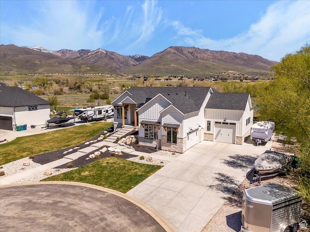 view of front facade featuring stone siding, a mountain view, concrete driveway, board and batten siding, and a front yard