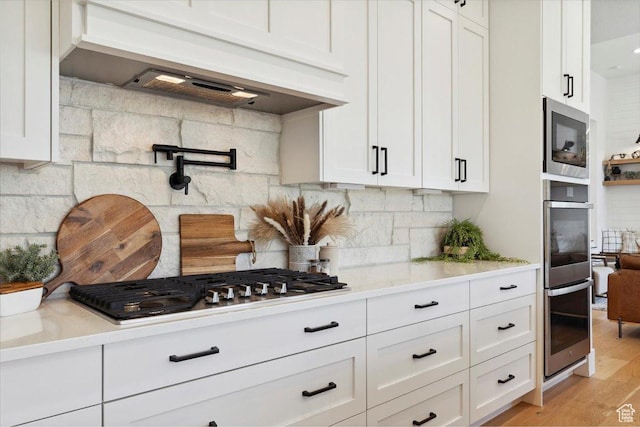 kitchen with custom exhaust hood, stainless steel appliances, and white cabinetry