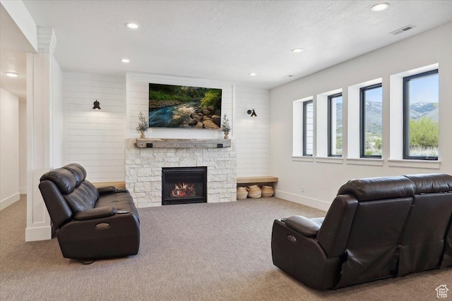carpeted living area with baseboards, a stone fireplace, visible vents, and recessed lighting