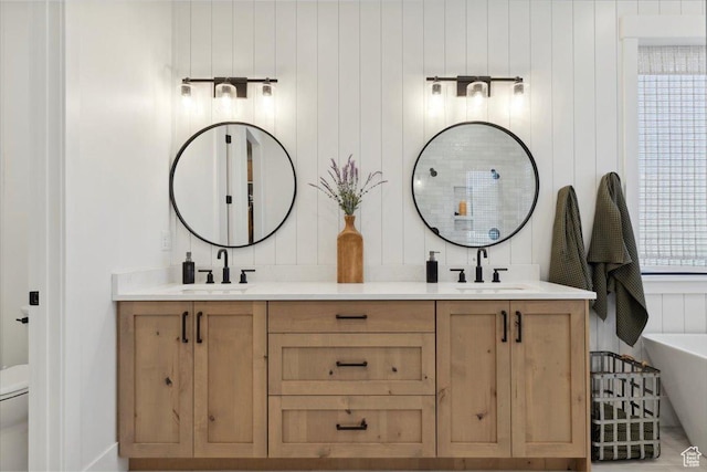 full bath with double vanity, toilet, a freestanding tub, and a sink
