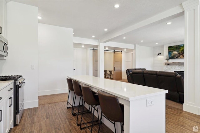 kitchen with gas range oven, a barn door, stainless steel microwave, and wood finished floors