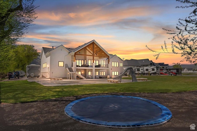 rear view of house with a patio area, a trampoline, a balcony, stairway, and a lawn