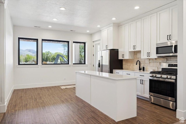 kitchen featuring stainless steel appliances, backsplash, light countertops, a center island, and baseboards