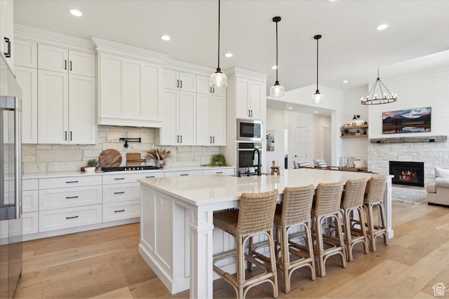 kitchen with a sink, stainless steel microwave, white cabinets, and light wood-style floors