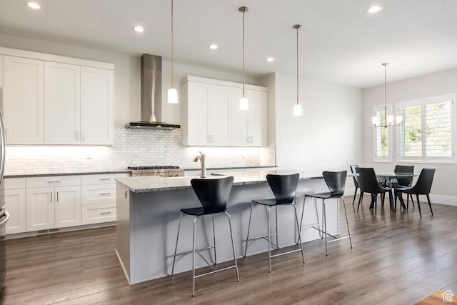 9293 S Regatta Ln, Cottonwood Heights, UT 84093 - kitchen featuring an island with sink, wall chimney exhaust hood, dark wood finished floors, light stone countertops, and backsplash