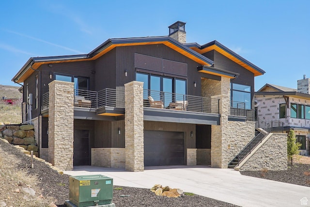 contemporary home featuring a balcony, a chimney, an attached garage, concrete driveway, and stone siding
