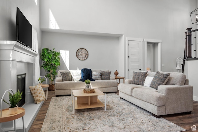living area featuring dark wood-type flooring, a towering ceiling, and a glass covered fireplace
