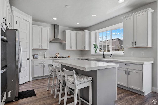 kitchen featuring a sink, a kitchen breakfast bar, wall chimney exhaust hood, dark wood-style flooring, and a center island