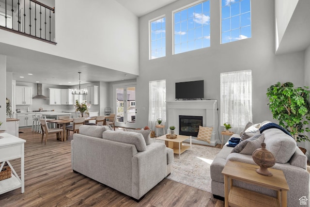 living area featuring a towering ceiling, a wealth of natural light, dark wood-style floors, a notable chandelier, and a glass covered fireplace