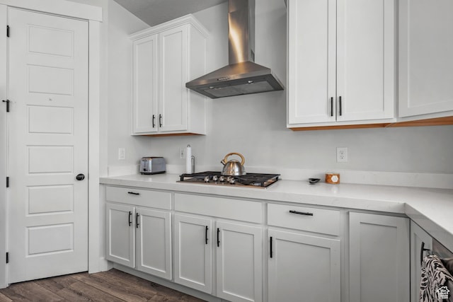 kitchen featuring stainless steel gas stovetop, dark wood finished floors, white cabinetry, wall chimney range hood, and light countertops