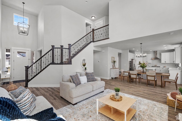 living area with stairs, an inviting chandelier, a high ceiling, and wood finished floors