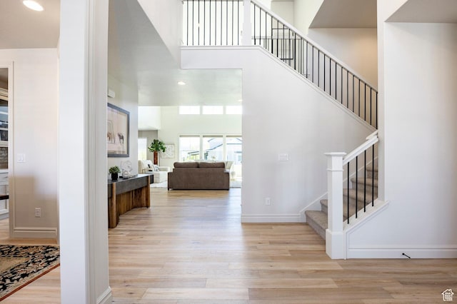 foyer featuring wood finished floors, stairs, baseboards, a towering ceiling, and recessed lighting