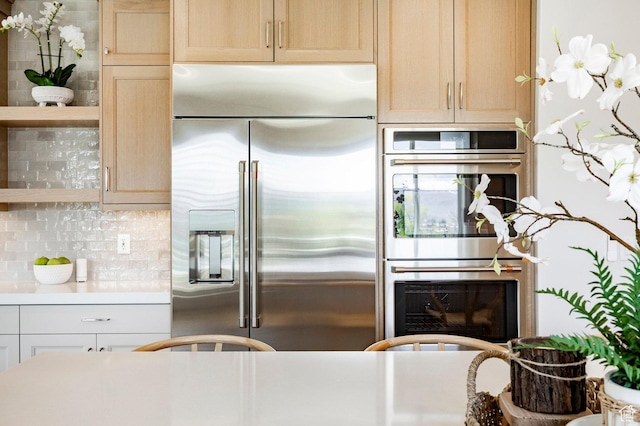 kitchen featuring appliances with stainless steel finishes, open shelves, decorative backsplash, light countertops, and light brown cabinetry