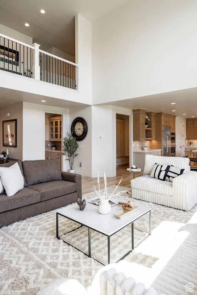 living area featuring a high ceiling, recessed lighting, light wood-style floors, and baseboards