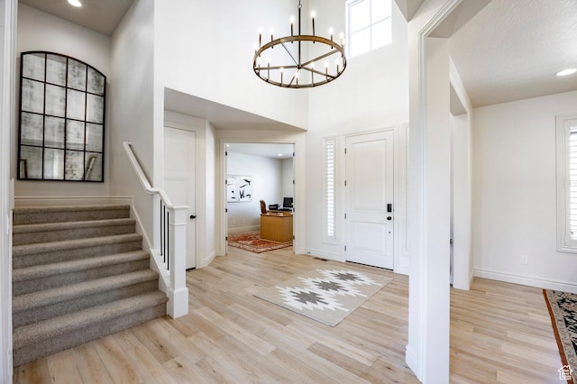foyer with a chandelier, light wood-style floors, baseboards, stairway, and a high ceiling