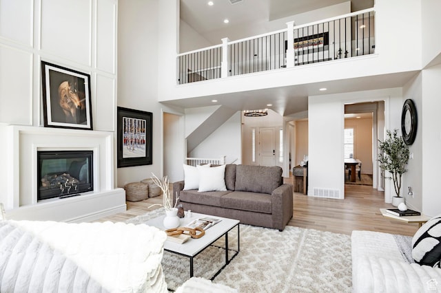 living area with light wood-style flooring, a high ceiling, a fireplace, recessed lighting, and baseboards