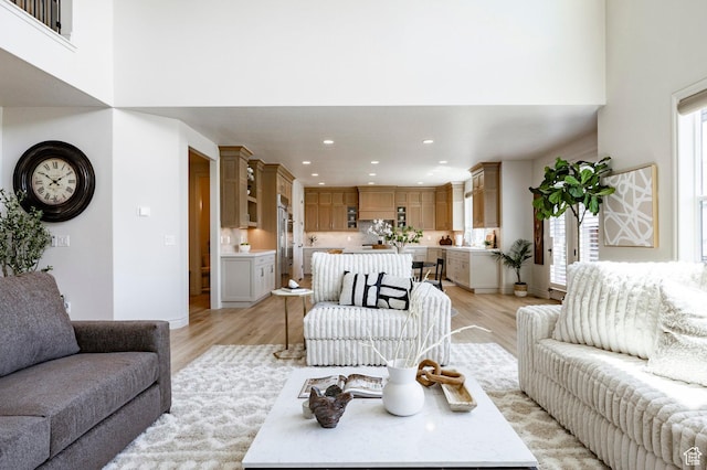 living room featuring light wood-type flooring, recessed lighting, a towering ceiling, and baseboards