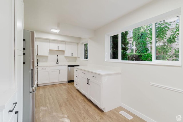 kitchen with a sink, stainless steel dishwasher, light wood-style flooring, and white cabinets