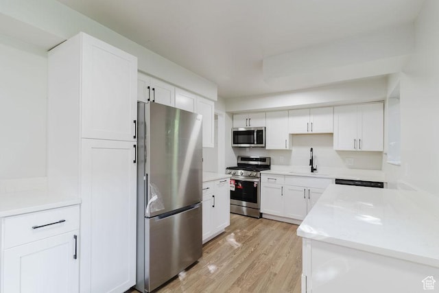 kitchen featuring stainless steel appliances, light wood finished floors, a sink, light countertops, and white cabinets