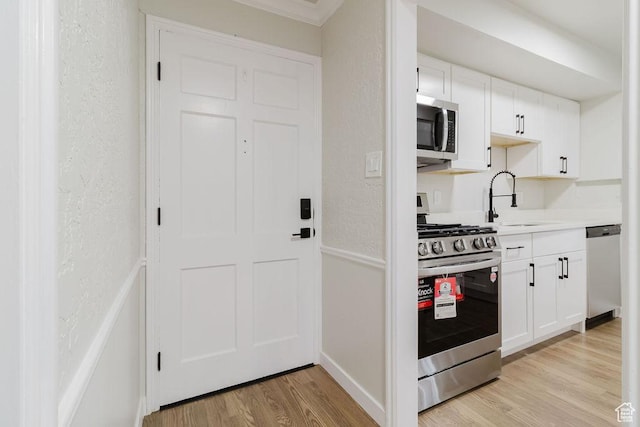 kitchen with light countertops, a sink, light wood-style floors, stainless steel appliances, and white cabinets