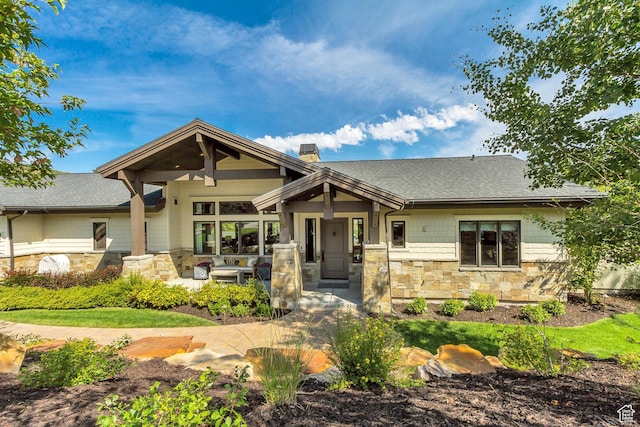 craftsman house with a shingled roof, a chimney, and stone siding