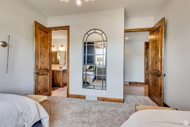 bedroom featuring an inviting chandelier, ensuite bathroom, visible vents, and wood finished floors