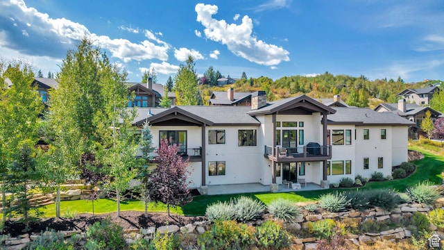 back of property featuring a residential view, a yard, a balcony, a patio, and stucco siding