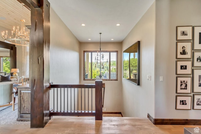 corridor with a notable chandelier, recessed lighting, baseboards, wood finished floors, and an upstairs landing
