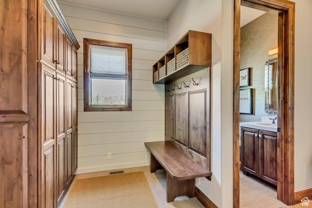 mudroom featuring visible vents, wooden walls, baseboards, and a sink