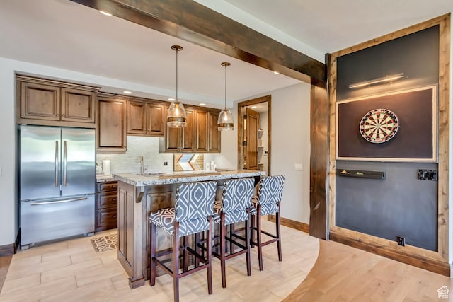 kitchen featuring a kitchen bar, a sink, pendant lighting, built in refrigerator, and decorative backsplash