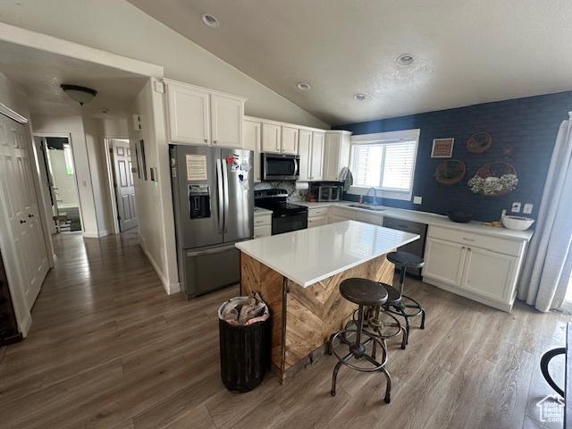 kitchen with stainless steel appliances, a sink, vaulted ceiling, white cabinetry, and wood finished floors
