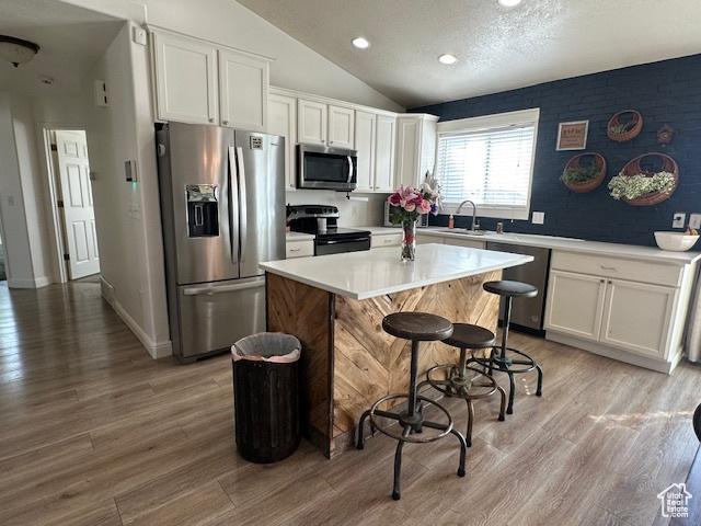 kitchen with stainless steel appliances, white cabinets, vaulted ceiling, a center island, and a sink