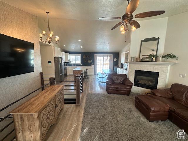 living area featuring a chandelier, light wood finished floors, a ceiling fan, a brick fireplace, and a textured ceiling
